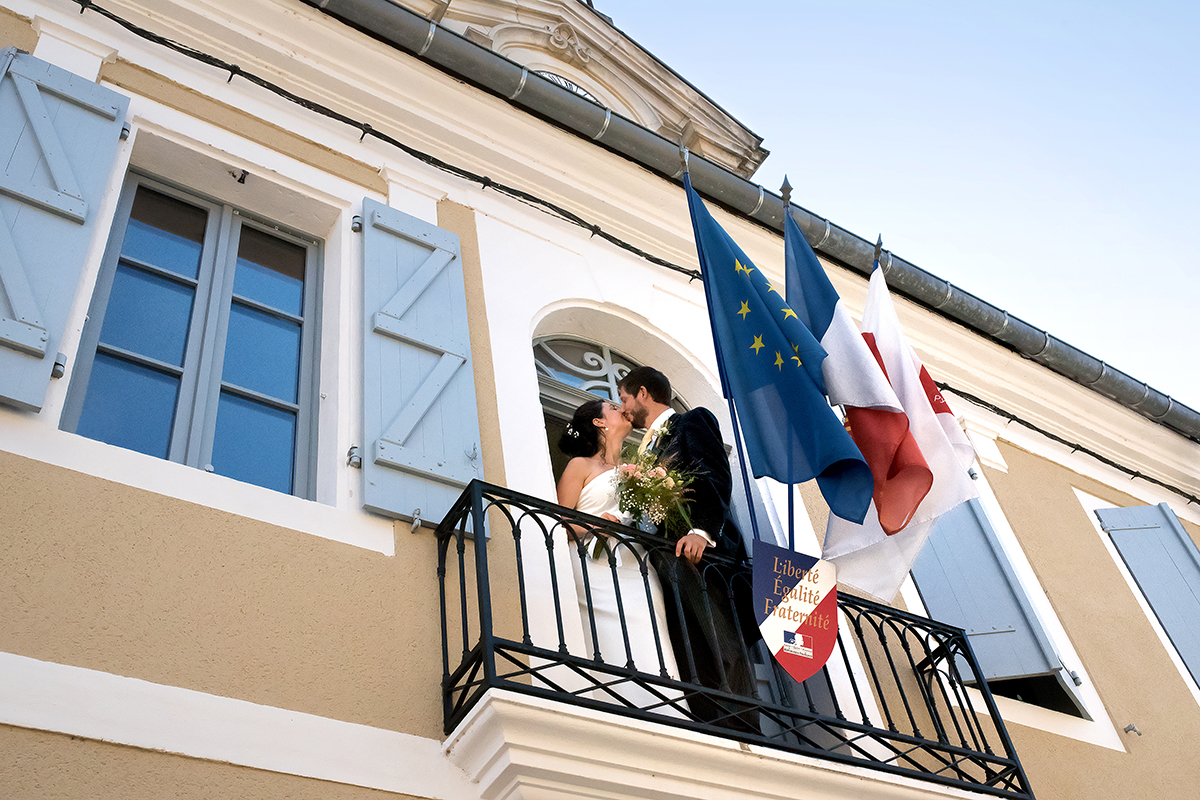 Baiser des mariés près des drapeaux français et européen placés sur le balcon de la mairie