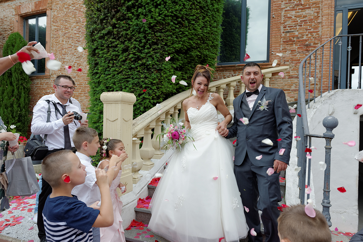 Les mariés descendent les escaliers de la mairie sous les pétales de fleurs lancés par les invités