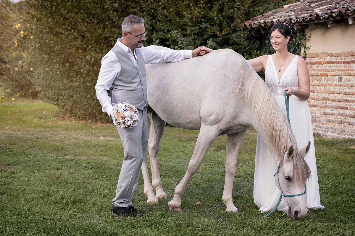 photographe mariage toulouse - Couple de mariés caressanr un cheval au domaine de Pindouls en région Toulousaine