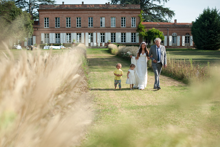 photographe mariage toulouse - Arrivée de la mariée auu bras de son père avec ses enfants à la cérémonie laïque au château Lavalade.