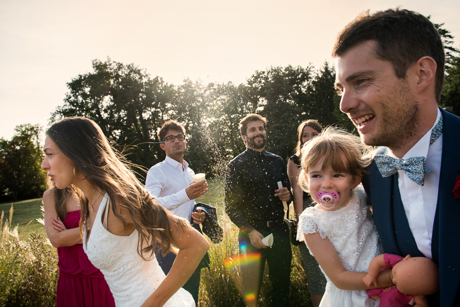 Les mariés avec leur enfant dans les bras courent pour éviter la profusion de pétales de fleurs lancés par les invités.
